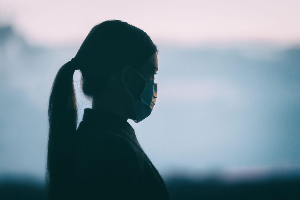 Woman wearing protective medical face mask stood alone looking out over surroundings